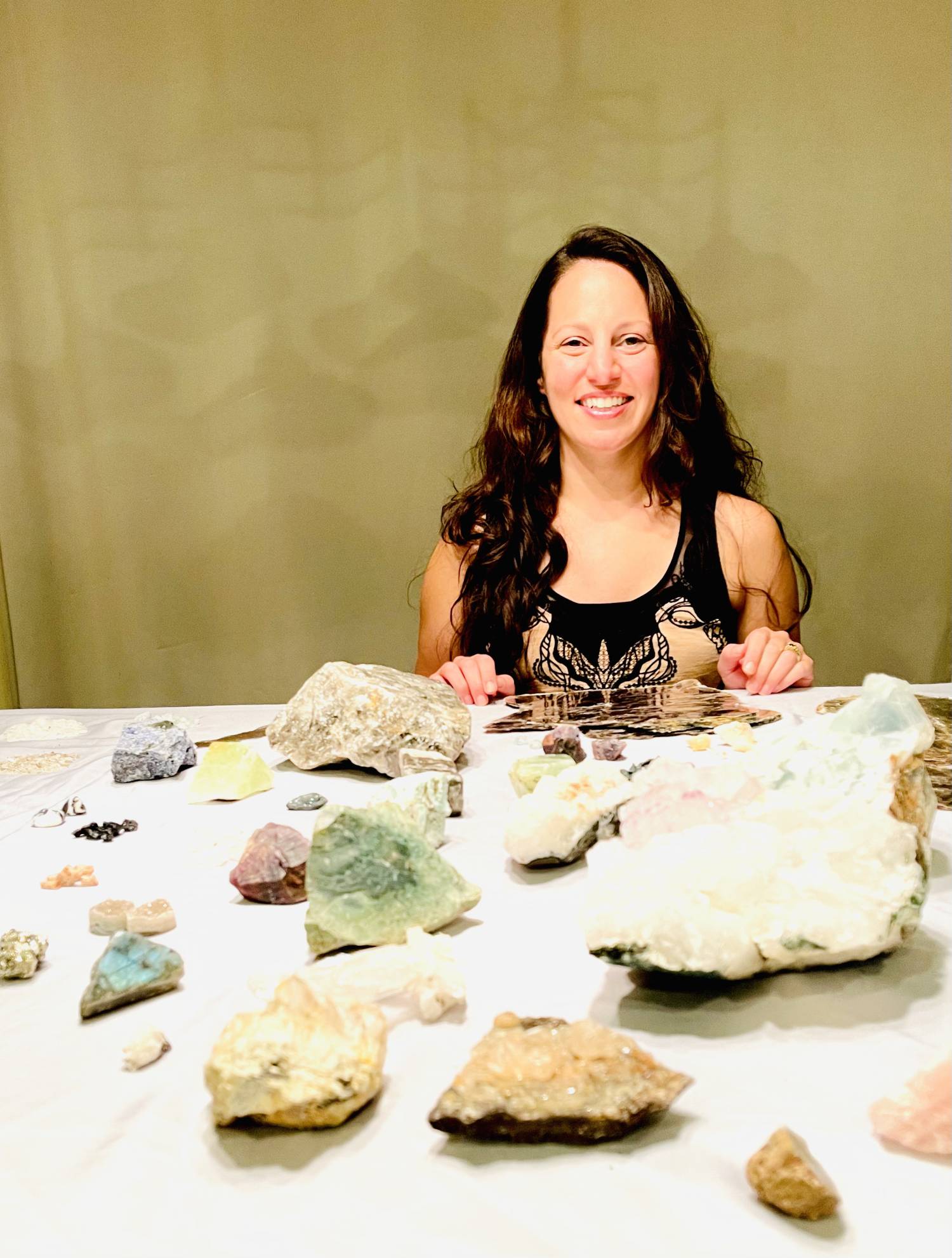 Photo of Tammy Campbell sitting in front of a table full of gemstones of varying shapes and sizes.