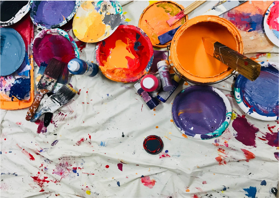 Colorful image showing paint tubs and artist tools on a paint splashed drop cloth.
